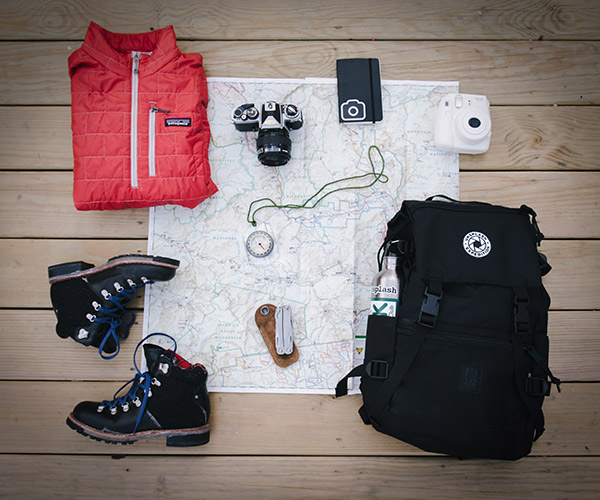 Outdoor hiking gear is meticulously arranged on a map. Essentials include a red jacket, black boots, a camera, compass, knife, black backpack, and metal water bottle. Ideal for adventurers seeking RV storage solutions to stow all this equipment while exploring the great outdoors.